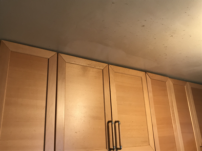 IKEA brand kitchen cabinets from 2004 below a dirty ceiling. The ceiling is partially cleaned, showing a contrast between the clean and dirty section.