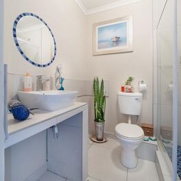 Clean bathroom featuring a toilette, mirror, glass shower doors, ceramic sink, and a picture above the toilette.